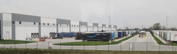 An endless building with an endless access road and many Amazon-branded trailers parked in front of it.