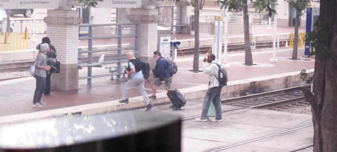 Two tracks with with people crossing them on some sort of concrete crosswalk.