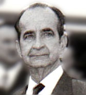 Kopfportrait eines etwa 60-jährigen Mannes im Anzug mit hoher Stirn, dunklen Haaren und einem ernsten Blick.