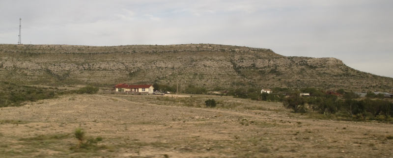 Cliffs in the background, then scattered houses, then brownish desert in the foreground.