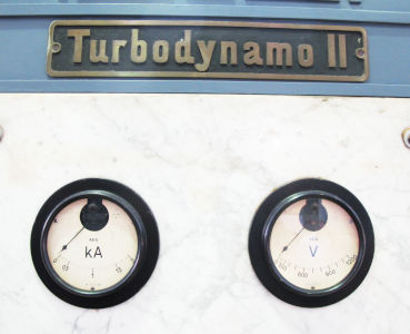 Ein in Kiloampere geeichter Strommesser und ein Voltmeter, rund, auf Marmorgrund, darüber en Blechschind in Sans-Serif: Turbodynamo II.
