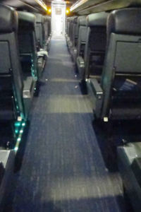 An aisle of a railway car, with only emergency light on.  At the far end, there's a bright patch.