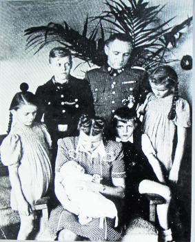 Familienfoto mit Mutter mit Baby am Arm und drei weiteren kleineren Kindern in der ersten Reihe, dahinter ein Mann in Uniform und neben ihn ein älterer Junge in etwas Uniformähnlichem.