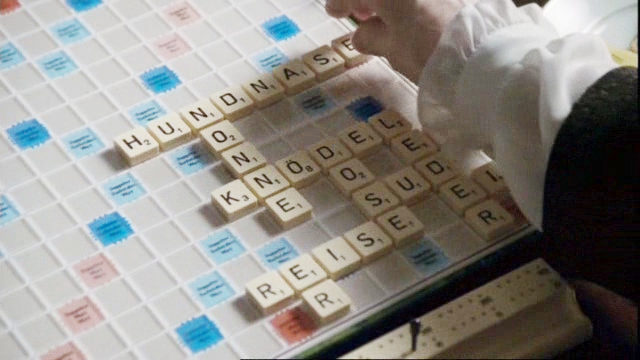 Ein Scrabble-Brett mit einigen gelegten Wörtern, eine Hand vollendet gerade „Hundnase“