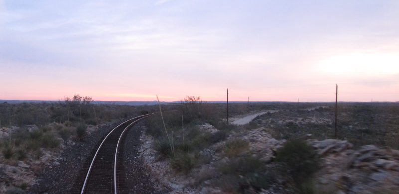 A reddish sky, rails leading away from it on stony ground