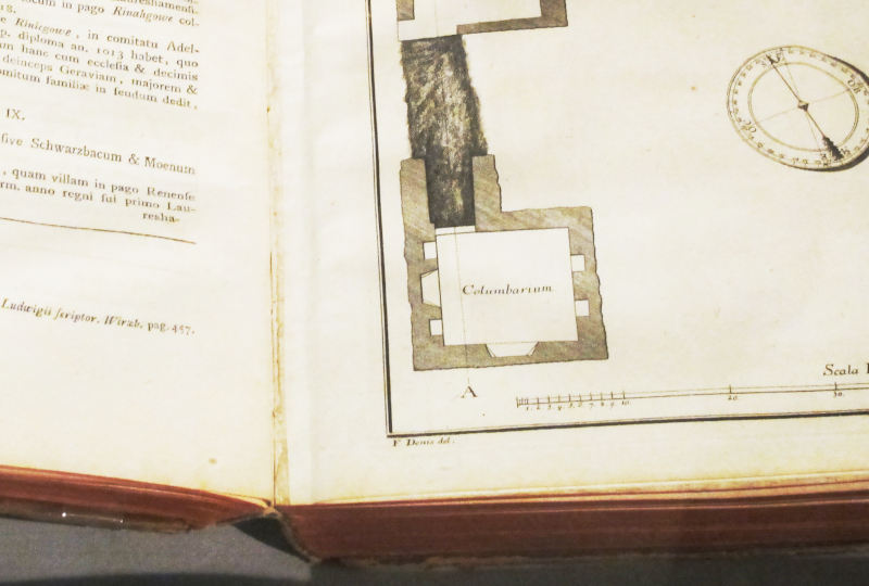 Ausschnitt eines aufgeschlagenen, etwas altertümlichen Buchs, Latein in Antiqua gesetzt.  Dazu eine Grabungsskizze mit einem also „Columbarium“ bezeichneten Raum mit einigen Nischen.