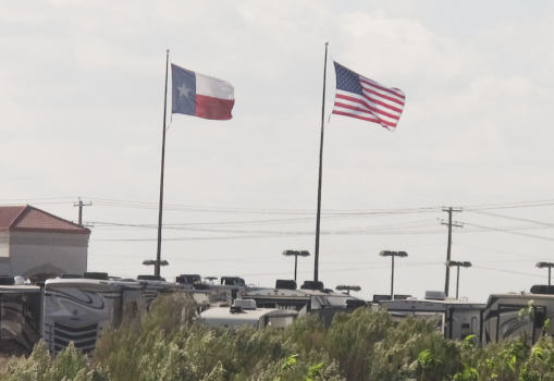 A US and a Texan flag, equal-sized, flying over a dealership for used mobile homes.