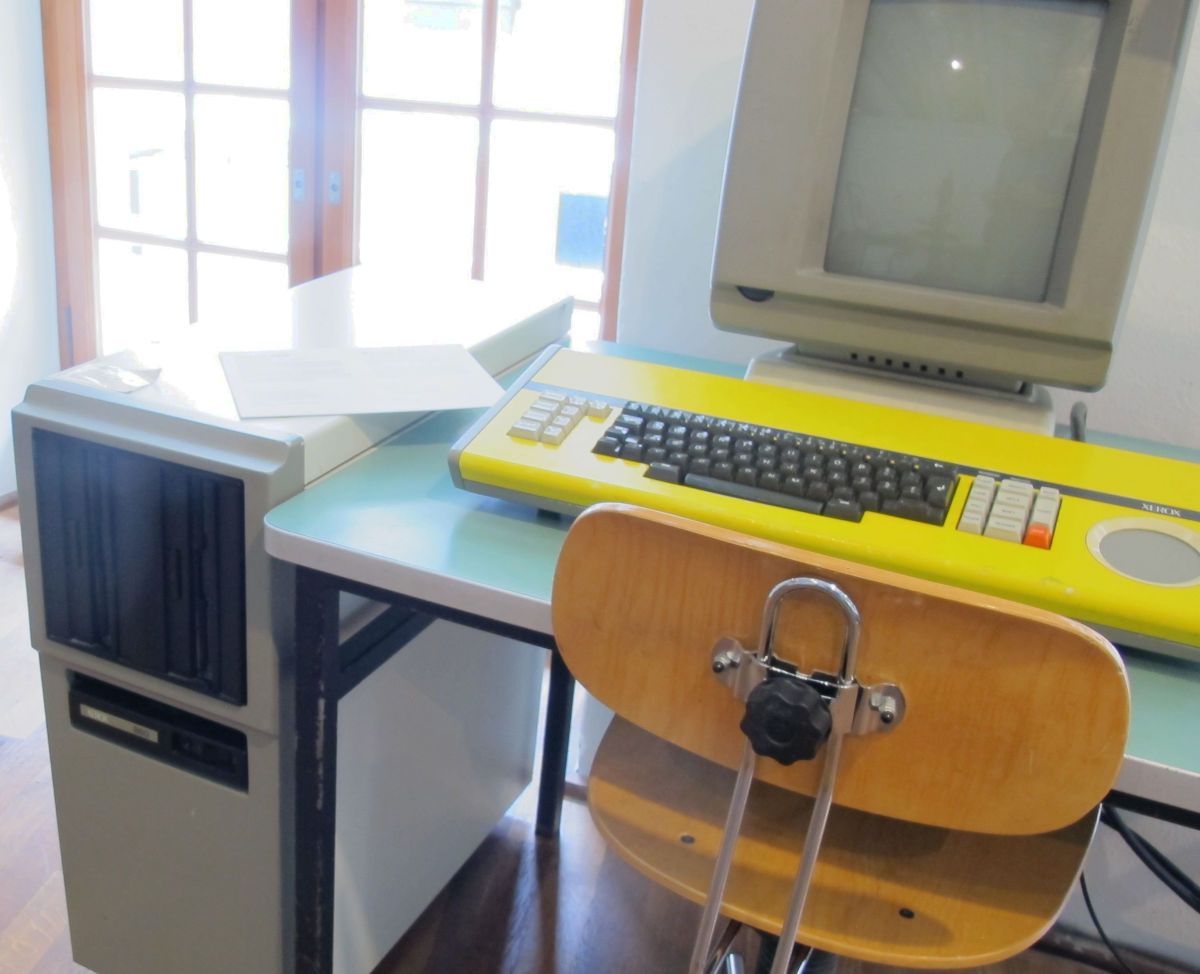 Ein schreibtischhoher Rechner neben einem Schreibtisch mit einem Hochkant-Monitor und einer großen gelben Tastatur.