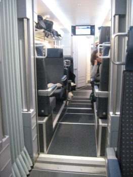 An aisle of a long distance train.  You can see some limbs of relaxed persons sticking out.