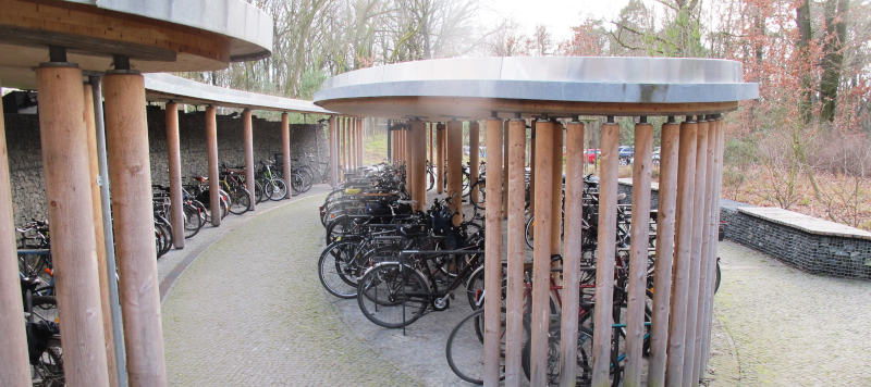 Geschwungen gebaute Fahrradständer für vielleicht 150 Fahrräder. Dach wie Trägersäulen sind sehr massiv.