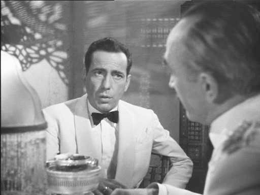 Schwarzweiß-Screenshot: Humphrey Bogart schaut sardonisch und hat den Mund halb geöffnet.