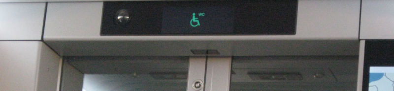 A green wheelchair logo with a small “WC” next to it above a sliding door of a train.