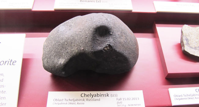 Ein rundlicher Stein mit vielleicht 10 cm Durchmesser und einer Delle in der Mitte, darunter eine Museumsbeschriftung: Cheliabynsk 2013