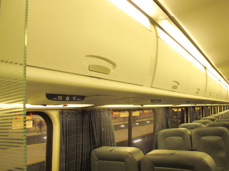 The interior of an open railway car; a long line of locker doors lines the ceiling.