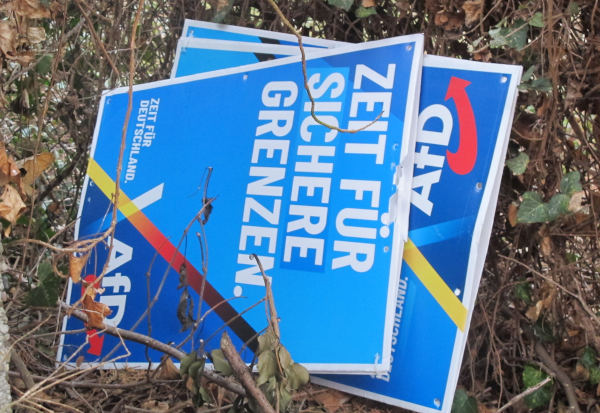 Zwischen Pflanzen liegende Papp-Plakate.  Auf dem vordersten steht: "Zeit für sichere Grenzen"