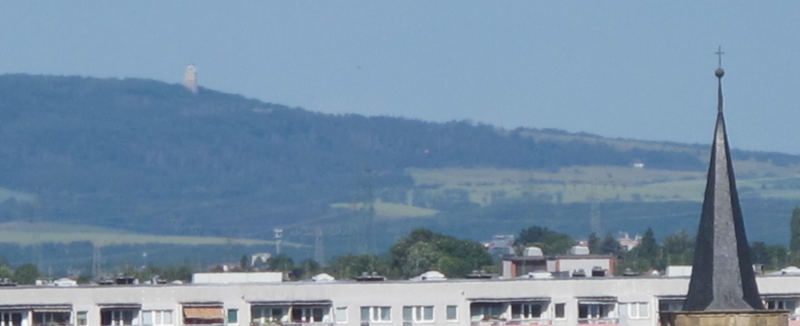 Ein Bergzug (der Ettersberg) etwas im Dunst verblasst hinter den obersten Fenstern von ein paar Mietshäusern im Vordergrund. Am Hang des Bergzugs ist ein Turm zu erkennen.