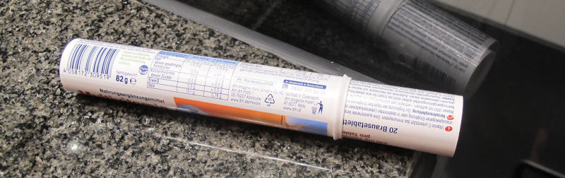 Zwei mit allerlei kommerziellem und medizinoioden Text bedruckte Rollen sind ineinandergesteckt und liegen auf dunklem polierten Granit oder einer ähnlichen Platte.