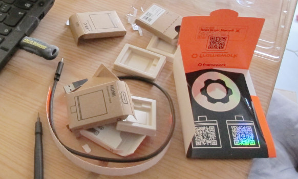 Scattered empty cardboard boxes about 5 cms in size, a USB cable, and some plastic on a table next to the edge of a notebook computer.