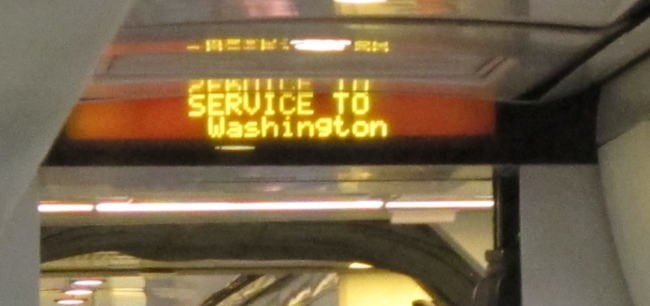 An old-fashioned, low-resolution LED display saying “SERVICE TO Washington” over a passage to the next railway car.