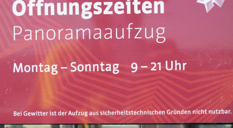 Auf einem roten Hintergrund steht: „Öffnungszeiten Panoramaaufzug (irgendwas)/Bei Gewitter ist der Aufzug aus sicherheitstechnischen Gründen nicht nutzbar“.