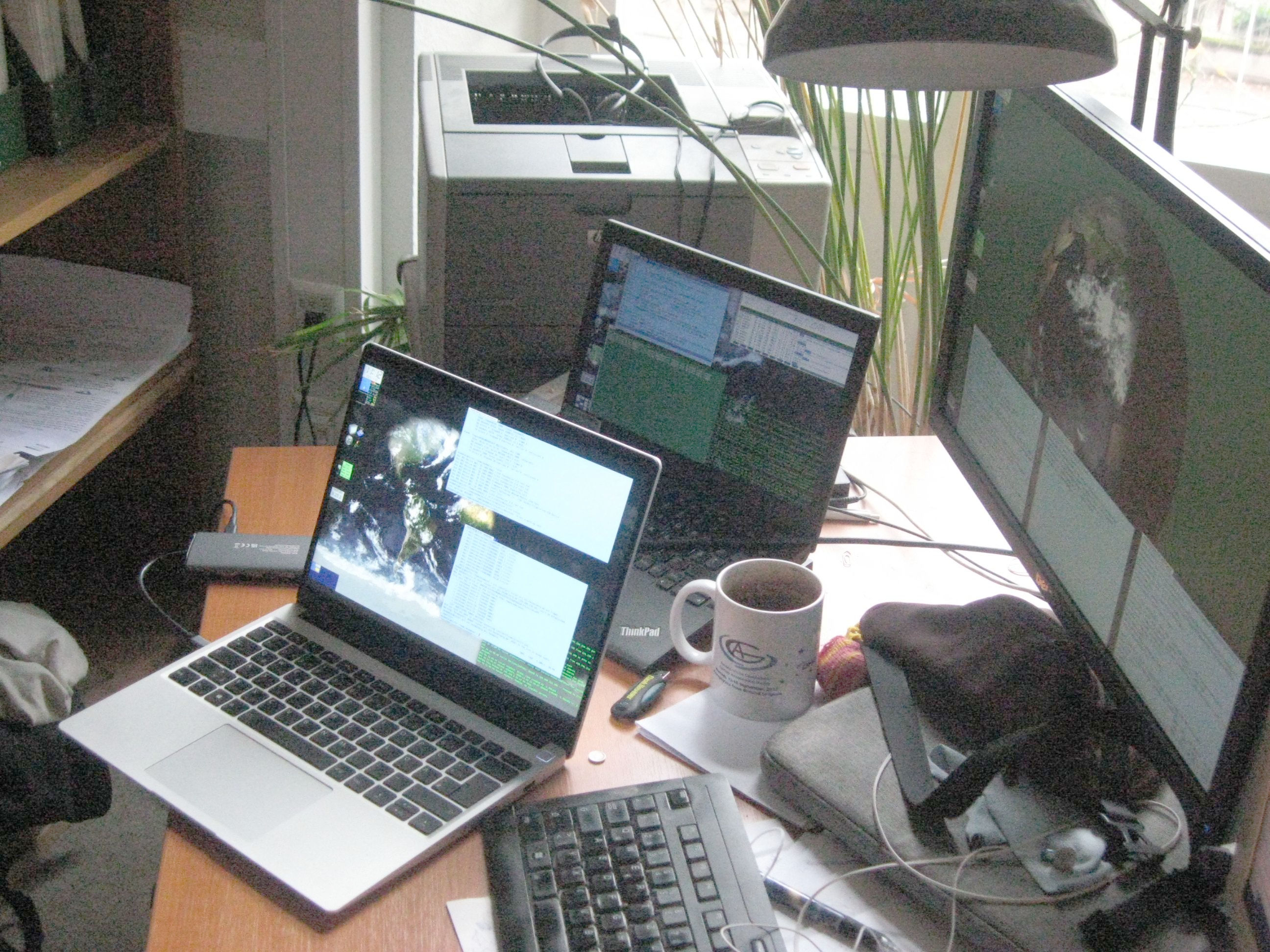 Zwo notebook computers with glowing displays next to each other. The front one has a much brighter screen.  A stationary monitor is behind both, also glowing quite a bit fainter than the front one.