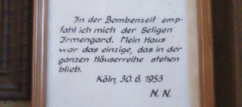 Eine gerahmte handschriftliche Notiz: „In der Bombenzeit empfahl ich mich der Seligen Irmengard.  Mein Haus war das einzige, das in der ganzen Häuserreihe stehen blieb.  Köln, 30.6.1953 N.N.“