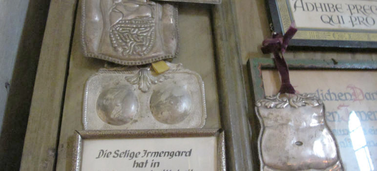 Metallene Halbreliefe eines Dünndarms, weiblicher Brüste und eines etwas fülligen Bauchs.