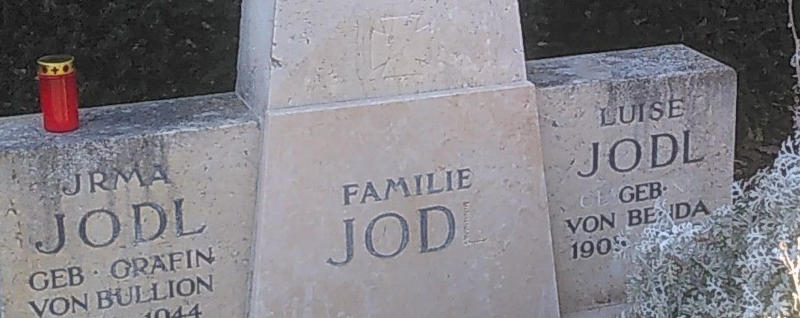 Detail aus einem Grabstein für Irma, Luise und Familie Jodl. Beim Schriftzug für die Familie fehlt ein L, und darüber ist schwach ein eisernes Kreuz im Halbrelief erkennbar.